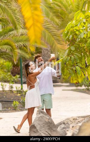 A young couple walks hand in hand, admiring nature in a lush tropical garden Stock Photo