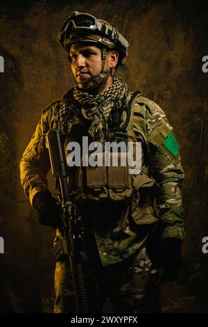A focused Latin American soldier clad in tactical gear stands ready, exuding confidence and preparedness in a rugged backdrop Stock Photo