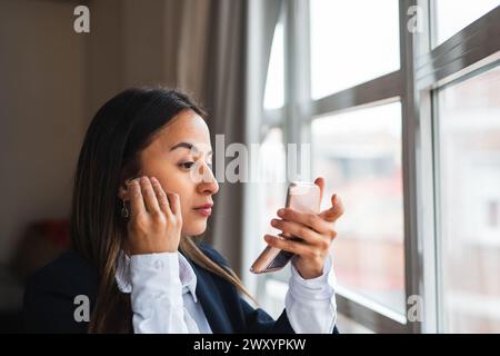 A businesswoman in a white shirt uses her mirror, checking her appearance by a window Stock Photo