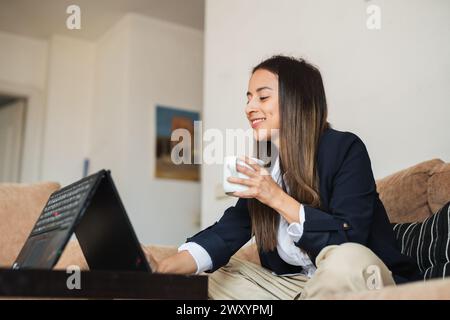 Young professional working on a laptop in a cozy home setting with a cup of coffee in hand Stock Photo