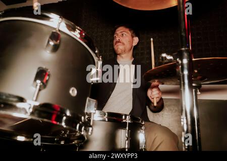 From below male drummer in a music band playing drums with focus, not looking at the camera. Stock Photo