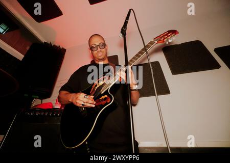 From below male musician with glasses stands, playing an acoustic guitar next to a microphone in a studio setting, looking away. Stock Photo