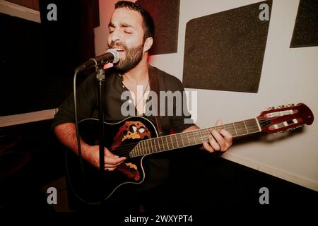Male musician passionately singing and playing an acoustic guitar at a live performance. Stock Photo