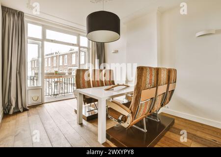 An elegantly designed modern dining room featuring distinctive chairs, a white table, and access to a balcony with urban views. Stock Photo