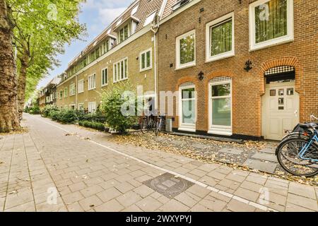A picturesque urban scene with a row of traditional brick houses and parked bicycles under the shade of green trees on a quiet street. Stock Photo