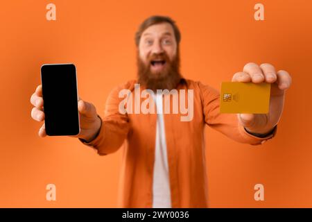 Cheerful bearded man showing cellphone screen and credit card, studio Stock Photo