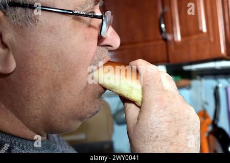 The picture shows an elderly man eating a bun. Stock Photo