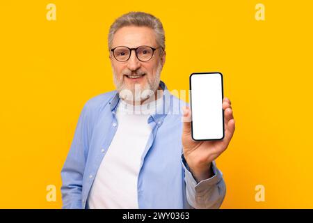 smiling senior man showing his smartphone empty screen, yellow backdrop Stock Photo
