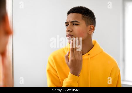 Concerned black teen guy examining face in the mirror Stock Photo