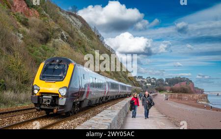 A train passes a middle-aged couple walking along the promenade on the seafront in Teignmouth, Devon, UK. Stock Photo