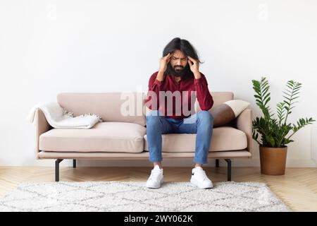 Man with headache sitting on couch at home Stock Photo