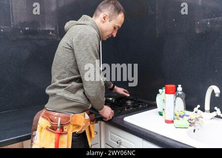 A gas engineer repairs a gas stove in the kitchen. The call of the master gas fitter to the house.  Stock Photo