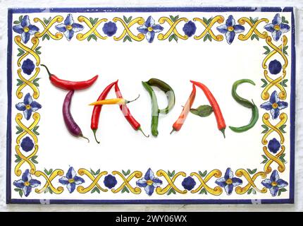 letter word TAPAS from red, green, yellow, purple chili pepper, vegetables letters, tapas bar, ceramic board in enamel or clay. pattern blue, yellow, Stock Photo