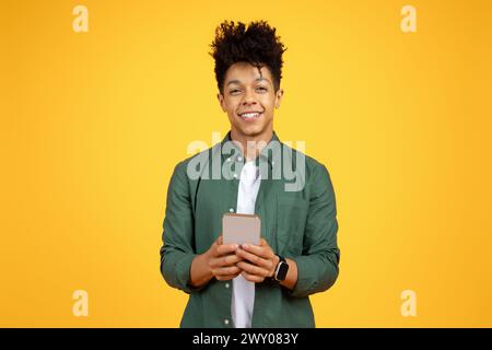Smiling young black man with phone on yellow Stock Photo