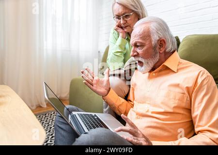 Senior couple at home reading bad news on laptop. Stock Photo