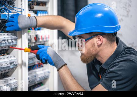 A male electrician works in a switchboard with an electrical connecting cable. Stock Photo