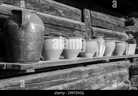 Some old clay pots on a wooden shelf with selective focus in black and white Stock Photo