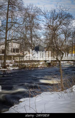 A River flowing through snow-covered forest surrounded by trees and houses Stock Photo