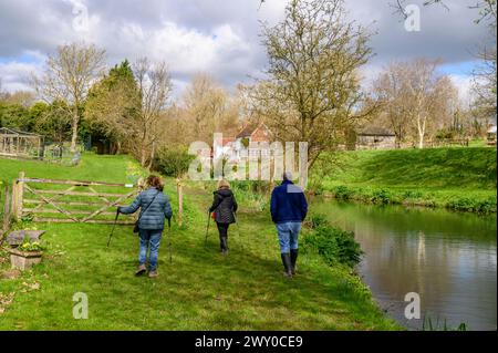 Three middle-aged persons walking along a stream towards farm houses in early spring in Nutbourne near Pulborough in rural West Sussex, England. Stock Photo