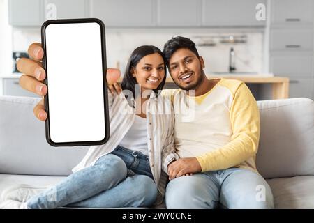 Indian Man and Woman Sitting on Couch Holding Up Blank Cell Phone Stock Photo