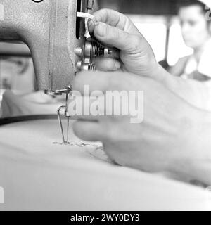 Socialist Republic of Romania in the 1970s. A seamstress using a sewing machine for an embroidery.  Close up of the worker's hands threading the machine. Stock Photo