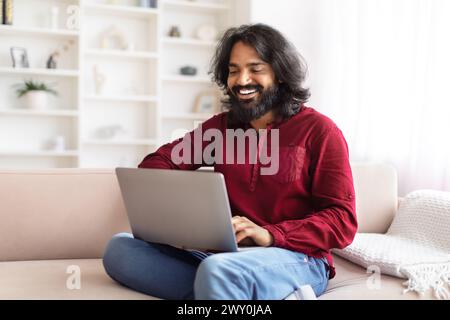 Man laughing while using a laptop on sofa Stock Photo