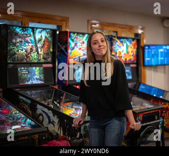 Portrait of a young smiling blonde leaning between pinball machines in a games and arcade room Stock Photo