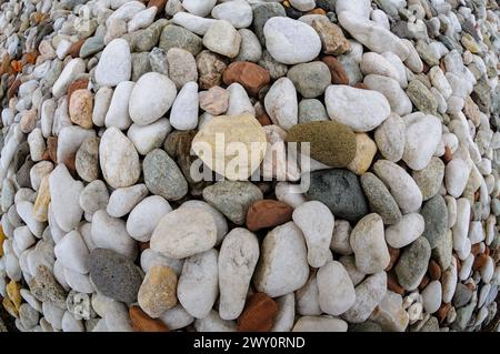 An assortment of rounded pebbles in various colors forms a spiral design on sandy ground. Stock Photo