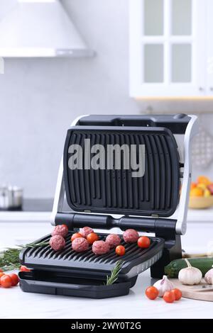 Electric grill with meatballs, tomatoes and vegetables on white table in kitchen Stock Photo