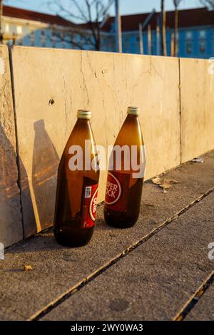 Two empty beer bottles on a street by a stone wall in sunset. Lisbon, Portugal. February 2, 2024. Stock Photo