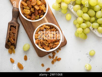 Sweet green raisins in bowl and scoop with grapes in wooden box on light kitchen background. Stock Photo