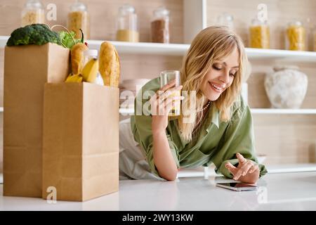 A woman sitting at a table in a kitchen, focused on her cell phone. Stock Photo