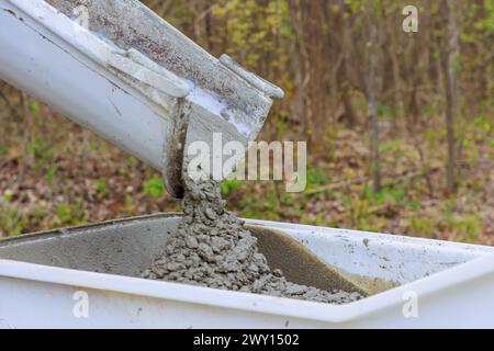 Construction site with wet cement coming from a cement truck chute into wheelbarrow track concrete buggy Stock Photo