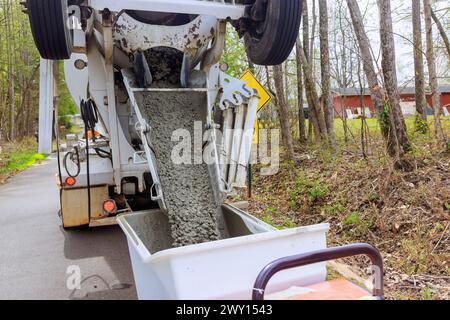 Wet cement coming down cement truck chute into a wheelbarrow track concrete buggy at construction site Stock Photo