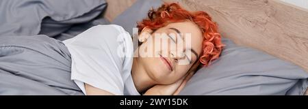 good looking red haired queer person in homewear napping in her bed at home, leisure time, banner Stock Photo