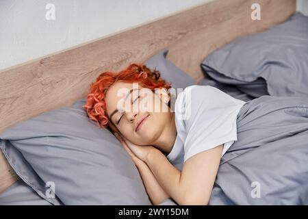 good looking red haired queer person in cozy homewear napping in her bed at home, leisure time Stock Photo