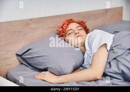good looking red haired queer person in cozy homewear napping in her bed at home, leisure time Stock Photo