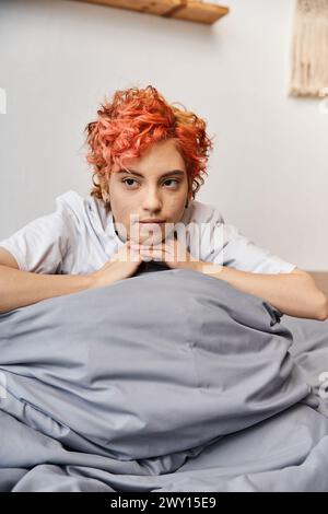 relaxing red haired queer person in homewear sitting on her bed at home and looking away, leisure Stock Photo