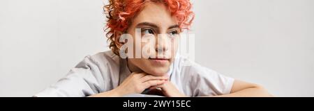 relaxing red haired queer person sitting on her bed at home and looking away, leisure time, banner Stock Photo