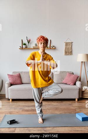attractive red haired queer person in vivid outfit meditating with closed eyes while at home Stock Photo