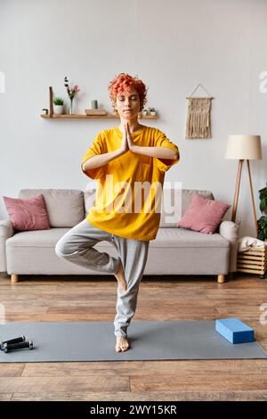 attractive red haired queer person in vivid outfit meditating with closed eyes while at home Stock Photo