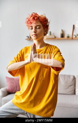 attractive red haired queer person in vivid outfit meditating with closed eyes while at home Stock Photo