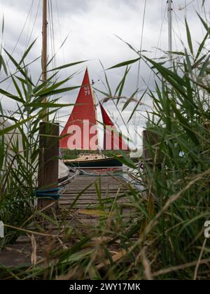 A sailing boat with red sails on the Norfolk Broads at Thurne, Norfolk, England, UK. Stock Photo