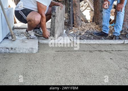 Installing new pavement or floor outside from large concrete tiles, closeup detail on male worker preparing stone block to fit over sand and gravel ba Stock Photo