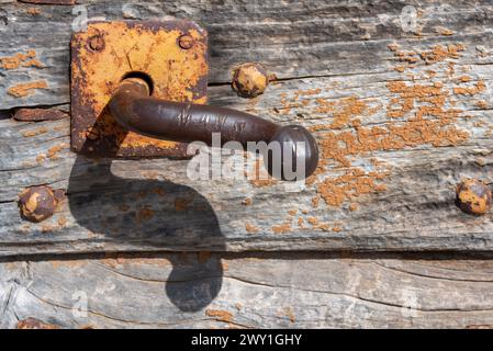 Close-up of old rusty iron handle on weather-damaged antique wooden door Stock Photo