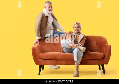 Mature couple sitting on sofa against yellow background Stock Photo