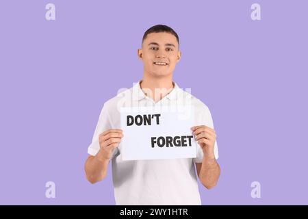 Young man holding paper with text DON'T FORGET on lilac background Stock Photo
