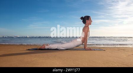 Yoga outdoors on beach, woman in upward facing dog pose on a sandy beach in the sun Stock Photo