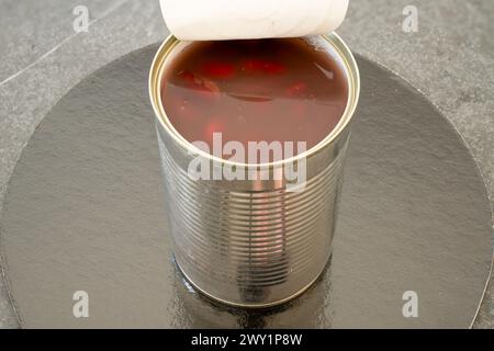 Close up of opened tin can with bent lid. Content of brown kidney beans and liquid can be seen. Stock Photo