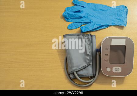 A blood pressure monitor and a pair of blue gloves are on a wooden table Stock Photo